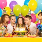 Group of joyful little kids celebrating birthday party and blowing candles on cake. Holidays concept.